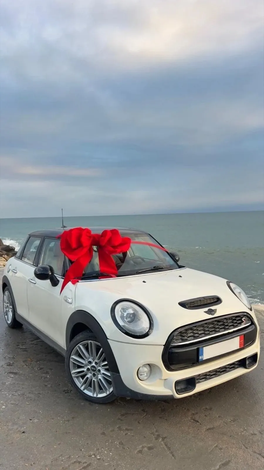 Бяло Mini с червена панделка на морския бряг